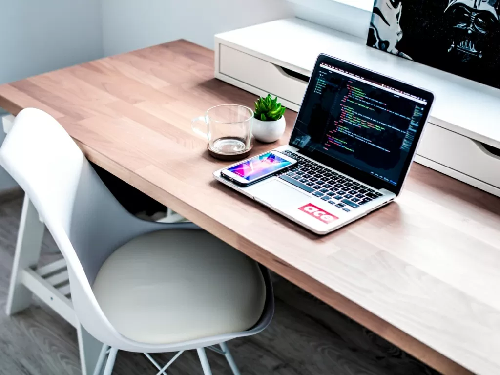 Laptop computer on top of desk with a chair slightly pulled out from under desk angled toward view of the observer.